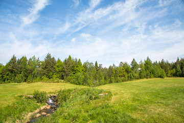 Fototapeta na wymiar Landscape on a golf course with green grass, forest, trees, beautiful blue sky and a small river and waterfall