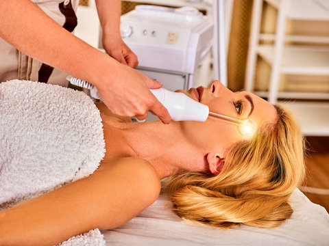 High frequency machine in spa salon. Young woman receiving electric darsonval facial massage after procedure at beauty room close up. Removal of acne from surface of face.