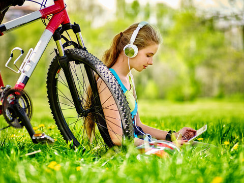 Bikes cycling girl. Girl rides bicycle. Girl wearing headset in cycling watch in pc tablet near bicycle. Cyclist looking pc tablet and listing music . Woman in social network communicates with friends