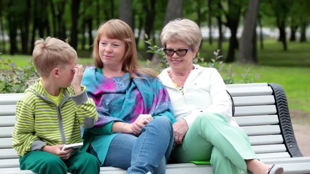 European elder grandma and adult woman listen the young boy while sitting in summer park