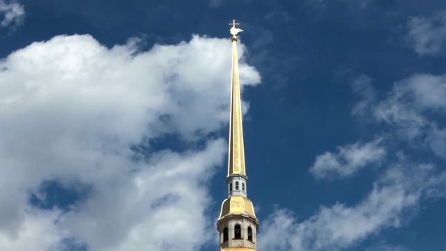 The spire of the Peter and Paul Fortress with cross and angel against the blue sky with running clouds. St. Petersburg, Russia