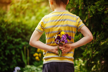 Child hands holding a bouquet pansies flower . Back view.Focus for flowers