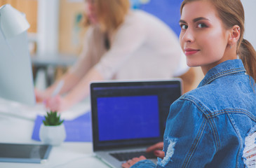 Two young woman standing near desk with instruments, plan and laptop