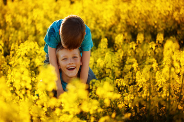 Two cute laughing boys hugging and having fun near the canola field. Adorable friends together on warm summer day. Brother love