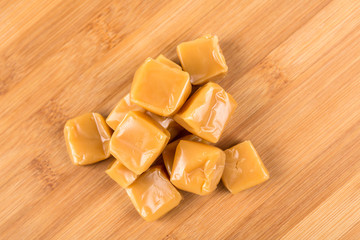 Chewy caramel cubes on a wood background