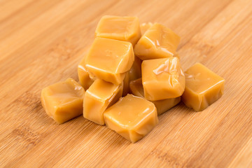 Chewy caramel cubes on a wood background