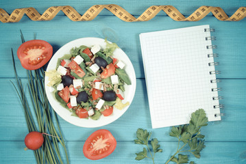 Vintage photo, Greek salad with vegetables, centimeter and notepad for notes, concept of nutrition and slimming