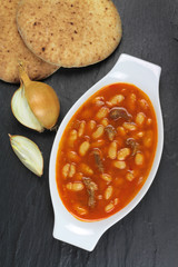 Traditional Turkish cuisine. Kuru Fasulye . Haricot Beans with onion and rustic bread on black stone background.