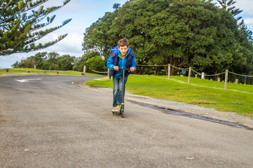 outdoor portrait of young happy preteen boy riding a scooter on natural background