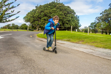 outdoor portrait of young happy preteen boy riding a scooter on natural background