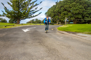 outdoor portrait of young happy preteen boy riding a scooter on natural background