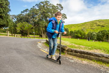 outdoor portrait of young happy preteen boy riding a scooter on natural background
