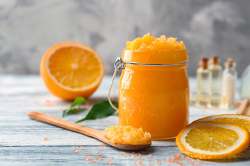Fototapeta na wymiar Glass jar with scrub, spoon and orange slices on wooden table
