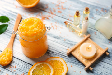 Glass jar with scrub, spoon, candle and orange slices on wooden background