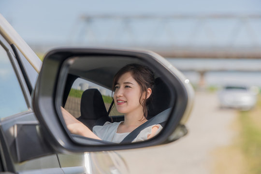 young female driver is reflected in a car side mirror.