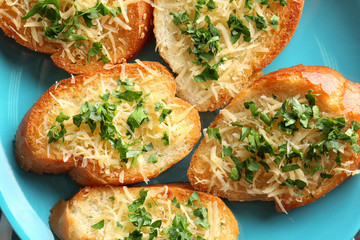 Tasty bread slices with grated cheese, garlic and herbs on plate