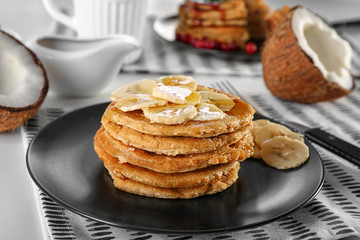 Stack of delicious coconut pancakes with sweet sauce and sliced banana on table