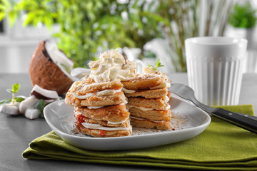 Stack of delicious coconut pancakes with butter cream, sweet sauce and shavings on table