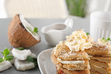 Stack of delicious coconut pancakes with butter cream, sweet sauce and shavings on table