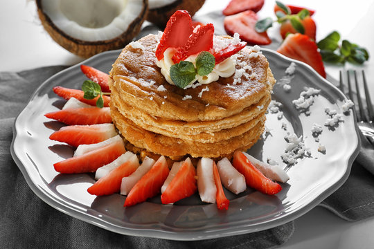 Stack of delicious coconut pancakes with strawberry and butter cream on napkin