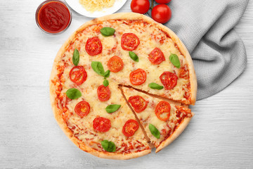 Delicious sliced pizza with tomatoes, basil and melted cheese on wooden background