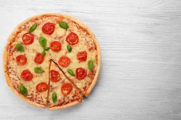 Delicious sliced pizza with tomatoes, basil and melted cheese on wooden background