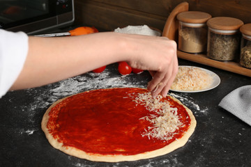 Female chef sprinkling cheese onto uncooked pizza on table