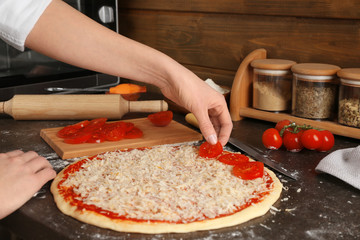 Female chef adding sliced tomatoes onto uncooked pizza on table