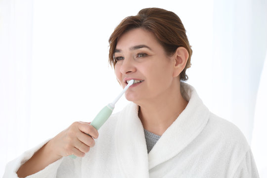 Senior woman cleaning teeth on light background