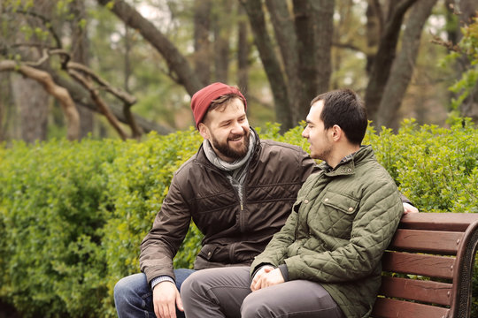 Happy gay couple sitting on bench in park