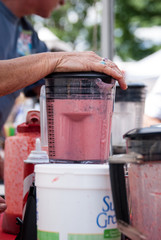 Hand holds lid on mixer as a strawberry smoothie is blended at local food festival