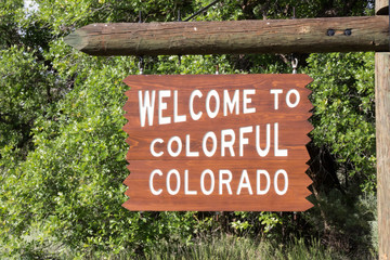 Fototapeta na wymiar Welcome to Colorful Colorado sign against green leaves