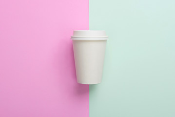Disposable takeaway (take out) coffee cup on light blue and pink background