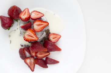 Delicious homemade chocolate cake with fresh red strawberries and cream sauce on white plate.