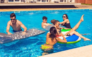 Party at smimming pool. Men and women playing in the pool with swimming circles and Swimming mattress. Summer rest and vacation