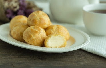 Homemade cream puffs filled vanilla custard cream or choux cream custard on wood table serve with tea in white pot or cup of coffee. Cream puffs,eclair, choux or puff pastry is french dessert.