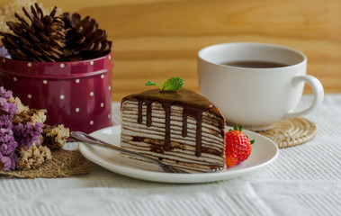Homemade chocolate crepe cake on white plate and napkin,cover cake by whipped cream,dark chocolate sauce topping,mint and lovely strawberry,tasty dessert for coffee break or tea time,fresh for summer.