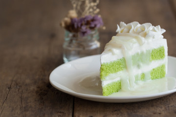 Pandan cake frosting by wipped cream topping with young toddy palm seed in coconut milk sauce on white plate put on wood table. Thai style dessert.