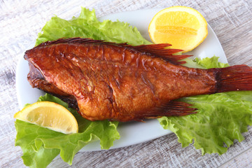 Smoked fish and lemon on green lettuce leaves on Wooden cutting board isolated on white background.