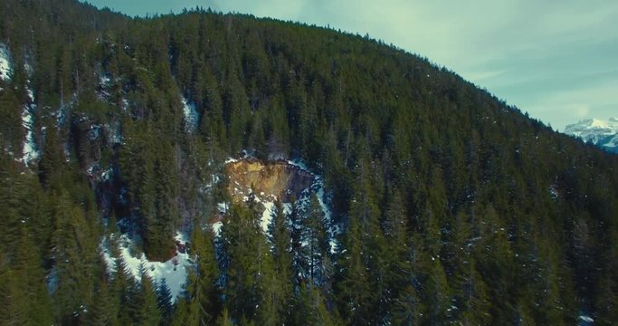 Luftaufnahme in verschneitem Bergwald mit Kamerafahrt zu H&ouml;hle im felsigen Berg, nah