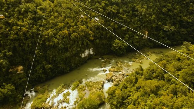 People have fun a zip line through a canyon with a river in the rainforest jungle. Aerial view, tourist attraction at the zipline attraction in the jungle on the island of Bohol. 4K video. Travel