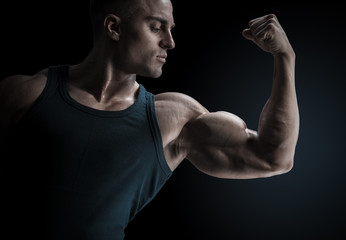 Young confindent muscular bodybuilder guy standing on black background and posing biceps muscle...