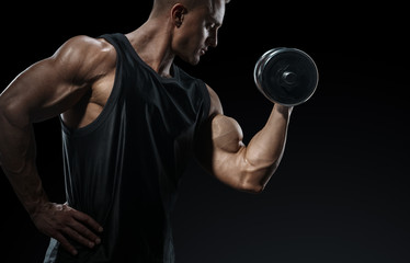 Fototapeta na wymiar Power athletic man in training pumping up muscles with dumbbell. Strong bodybuilder with perfect deltoid muscles, shoulders, biceps, triceps and chest. Close-up of a power fitness man.