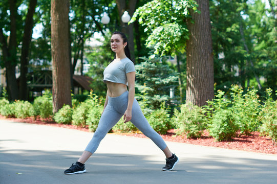 Beautiful brunette girl exercising in a green park. Training in nature. A healthy lifestyle. Sportswear. Happy girl.