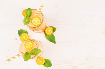 Orange citrus kumquat  fruit smoothie in glass jars with straw, mint leaf, cute ripe berry, top view. White wooden board background, copy space.