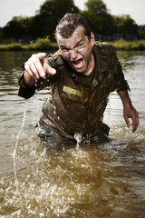 Wet and dirty angry soldier in uniform in river
