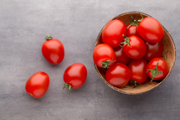 Small plum tomatoes in a wooden bowl on a gray background.