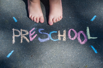 Preschool written with colourful chalks with child feet, top view. Preschool concept.
