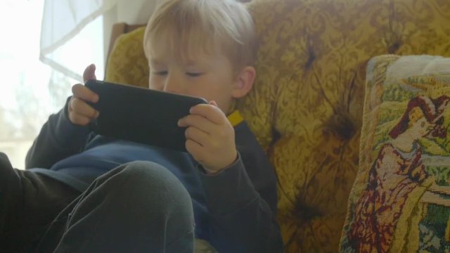 Adorable little kid plays on a phone while sitting on a couch in a living room