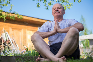 Naklejka na ściany i meble Yoga at park. Senior man with mustache with namaste sitting.Concept of calm and meditation.